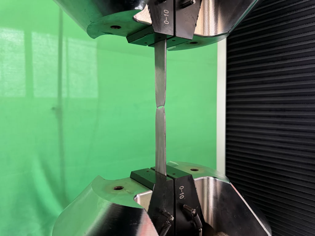 Flat tensile specimen fractured in the reduced section, still held in wedge grips